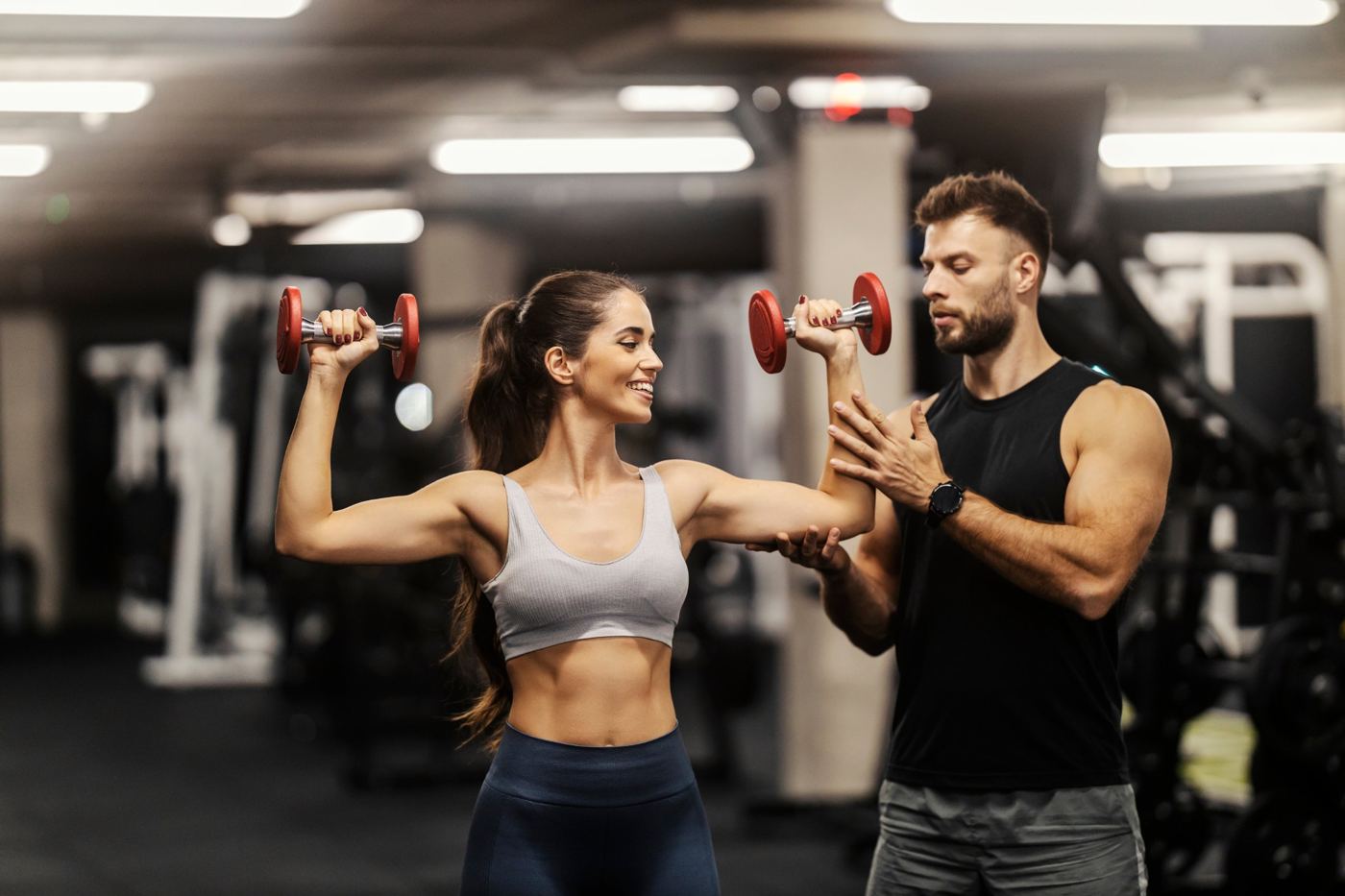 A personal trainer guiding a woman lifting dumbbells