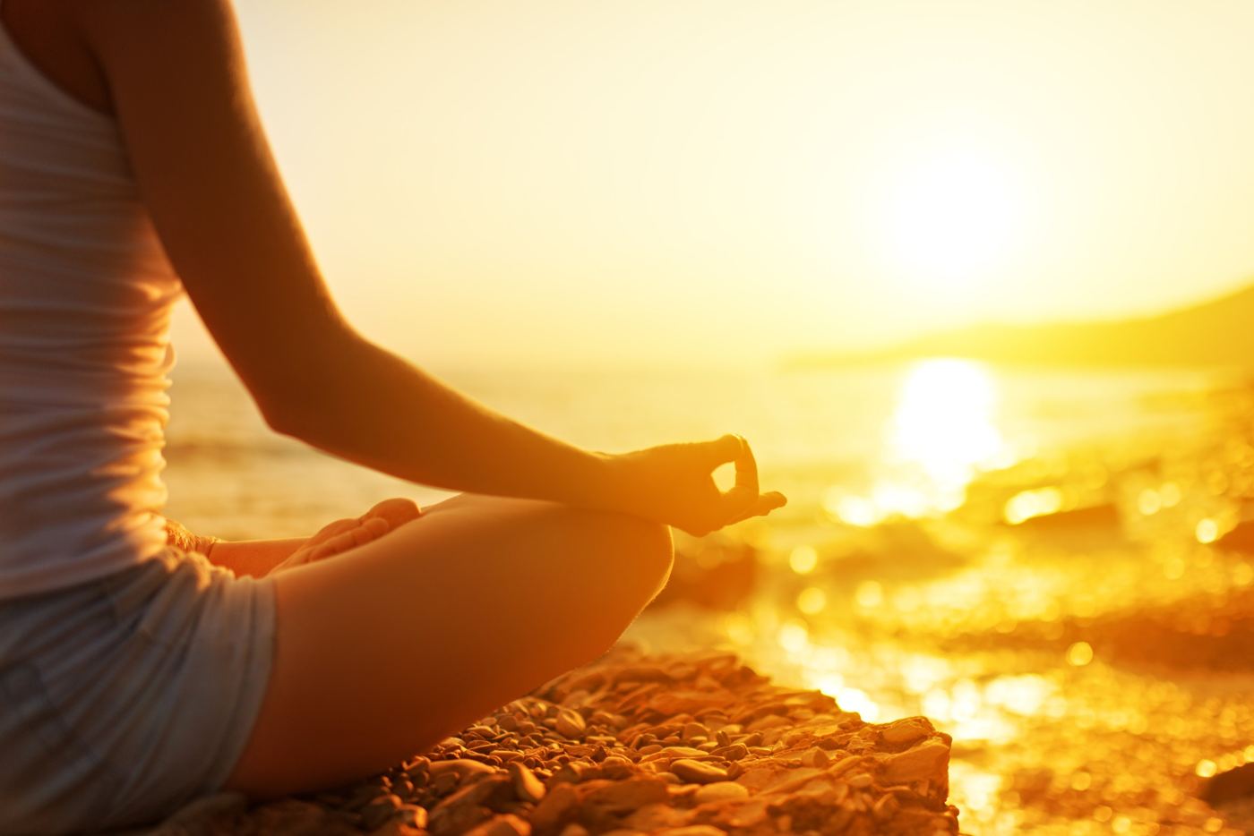 A woman meditating on a beach at sunset